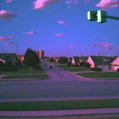 an empty street with houses in the background and a traffic light on one corner, at dusk