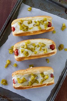 three hot dogs with toppings on a baking sheet, ready to be cooked in the oven