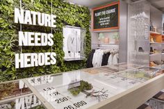 the inside of a clothing store with green plants on the wall and clothes displayed in glass cases