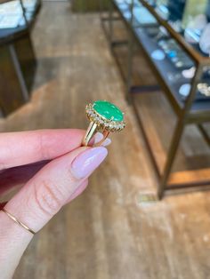 a person holding a ring with a green stone on it in front of some shelves