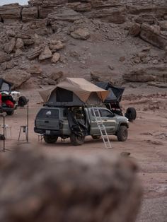 an suv parked next to a tent on the side of a rocky hill with another vehicle in the background