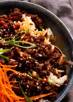 a bowl filled with meat and carrots on top of a bed of white rice