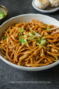 a bowl of noodles with chopsticks in it on a black table next to other dishes