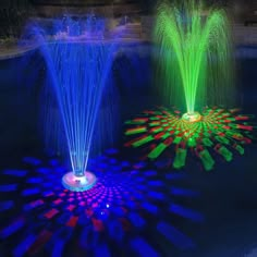 two colorful fountains in the middle of a pond with lights on top and water around them