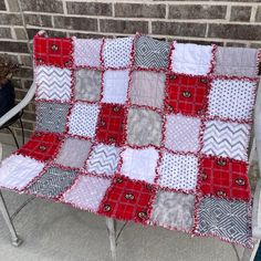 a red and white quilt sitting on top of a metal bench next to a brick wall