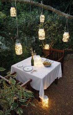 some mason jar lights hanging from a tree branch over a table with food and drinks on it