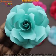 a hand holding a blue paper flower in it's left hand with other flowers behind it