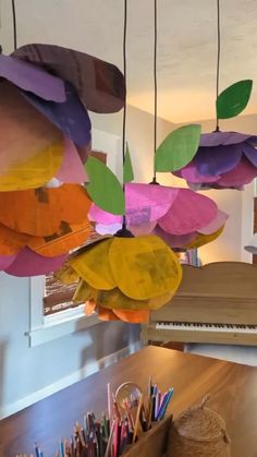 colorful paper flowers hanging from the ceiling in a room with a piano and pencils