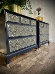 an ornately decorated dresser with gold accents on the doors and drawers, sits in front of a potted plant