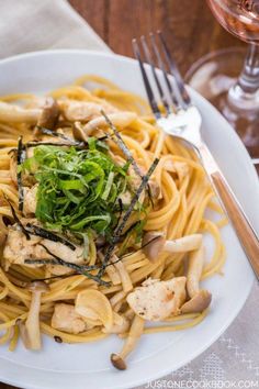 a white plate topped with pasta and chicken next to a glass of wine on top of a wooden table