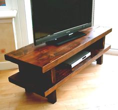 a flat screen tv sitting on top of a wooden stand in front of a window