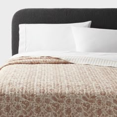 a bed with white pillows and brown bedspread on top of the headboard