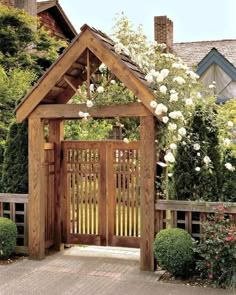 an open wooden gate with white roses growing on the top and bottom, in front of a house