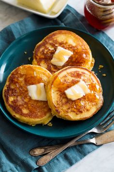 three pancakes with butter and syrup on a blue plate next to silverware, forks and cheese cubes