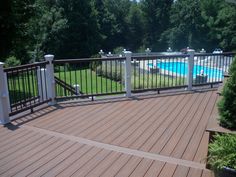 a wooden deck with railings next to a swimming pool and trees in the background