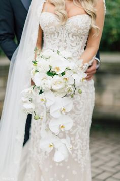 a bride and groom standing next to each other in front of a tree with white flowers