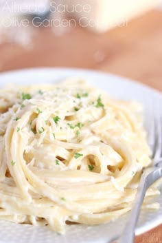 a white plate topped with pasta and parsley on top of a wooden table next to a fork