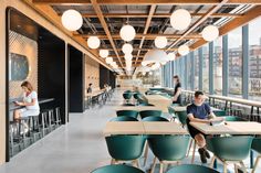 people are sitting at tables in an open area with lots of windows and green chairs