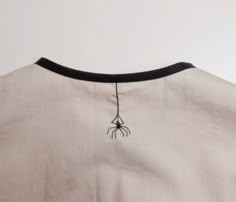 the back of a white shirt with a black spider on it's chest and neck