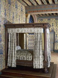 a four poster bed with drapes and curtains on the sides, in front of an ornate wallpapered ceiling