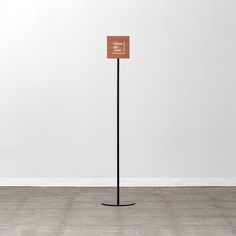 a wooden sign on a black pole in front of a white wall and wood floor