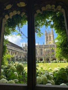 the view from inside an old building looking out onto a garden with white flowers and trees