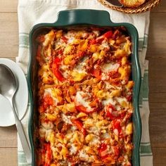 a green casserole dish filled with pasta and sauce on top of a wooden table