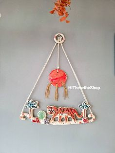 a wall hanging with an orange and black tiger on it's side, in the shape of a pendulum