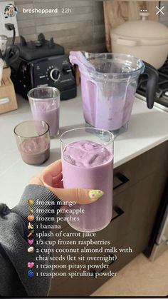 a person holding up two glasses with purple liquid in them on a kitchen counter top