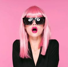 a woman with pink hair and black sunglasses on her face is making a funny face