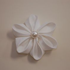 a white flower with a pearl in the center on a beige table cloth background, ready to be used as a brooch or lapel