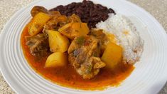 a white plate topped with rice and meat covered in gravy next to beans