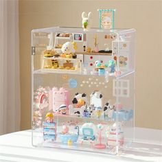 a clear shelf filled with toys on top of a white table next to a wall