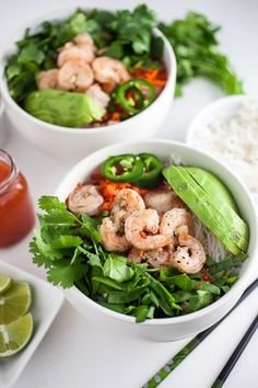 two white bowls filled with shrimp and veggies next to rice, cilantro