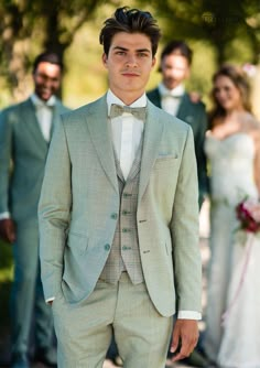 a man wearing a suit and bow tie standing in front of other groomsmid