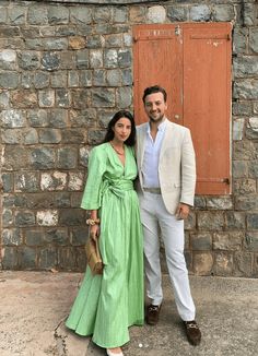 a man and woman standing next to each other in front of a stone building with wooden doors