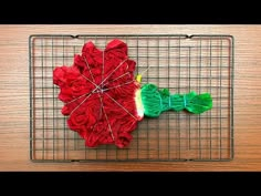 a red flower sitting on top of a wire rack next to a piece of yarn