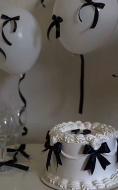 a white cake with black ribbon and balloons