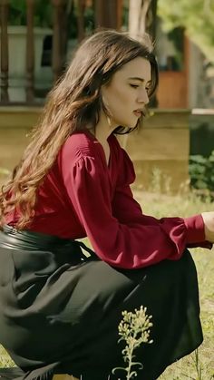 a woman in a red shirt and black skirt sitting on the ground