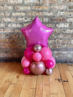 a pink and gold balloon tree with star shaped balloons on the top, in front of a brick wall