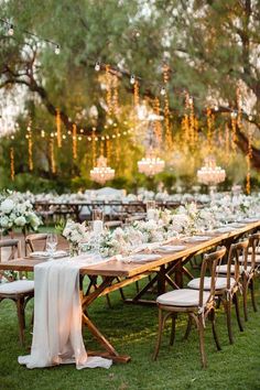 a long table set up with white flowers and greenery for an outdoor wedding reception