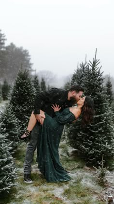 a man and woman kissing in the middle of a christmas tree lot with snow falling on them