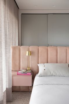 a bedroom with a pink headboard and white bedding, along with a gold lamp