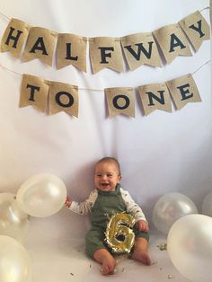 a baby sitting on the floor with balloons and streamers in front of him that say halfway to one