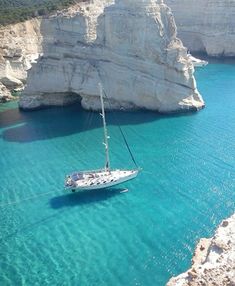 a sailboat floating in the blue water next to white cliffs