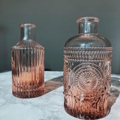 two glass vases sitting on top of a marble countertop next to each other