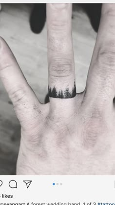 a person's hand with a ring on it and trees in the middle of their fingers