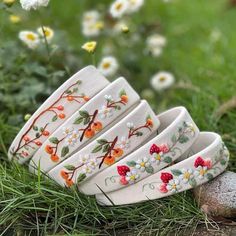 four white bracelets with red and yellow flowers on them are sitting in the grass