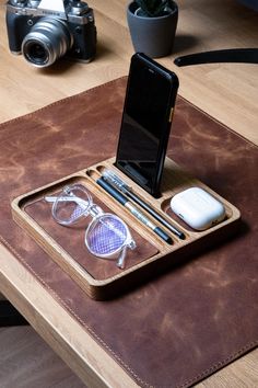 a cell phone, pen and glasses on a tray with a camera in the background