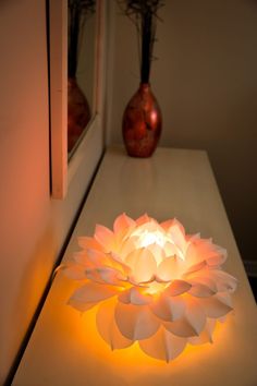 a lit up flower sitting on top of a table next to a vase with flowers in it